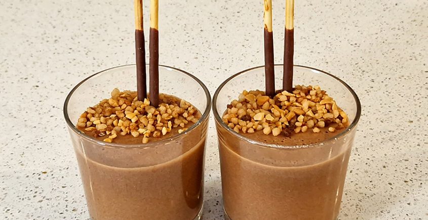 Chocolademousse praliné in een glas met twee mikado stokjes en nougatine